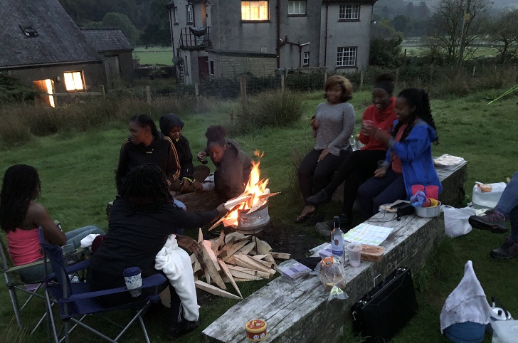 A group of women sitting around a campfire in the countryside