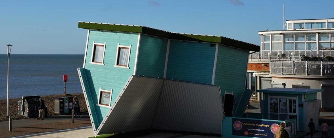 A blue terraced house sits upside down in an art installation by the sea