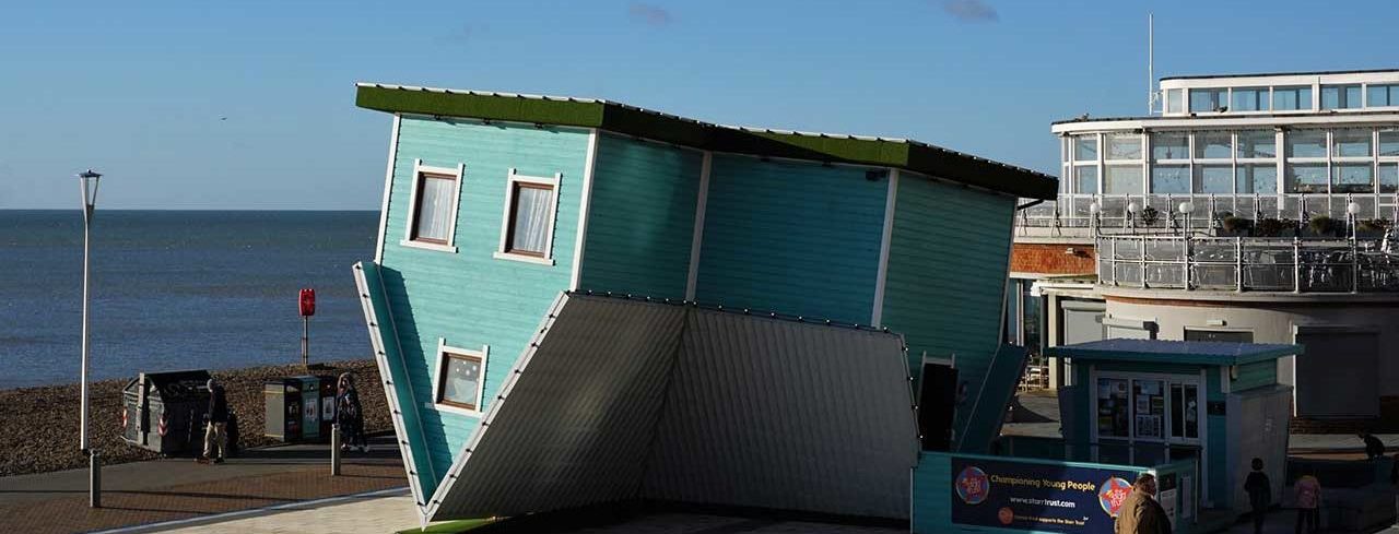 A blue terraced house sits upside down in an art installation by the sea