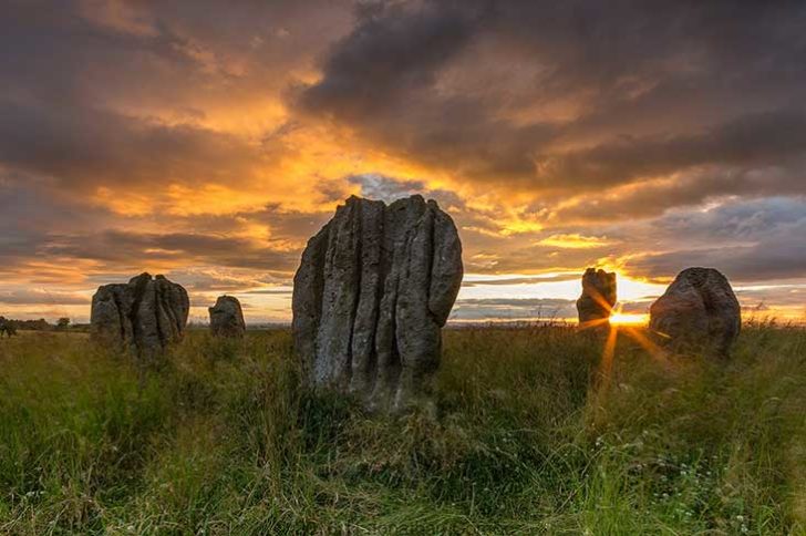 Dramatic ridged stones in long grass in front of an orange sunset