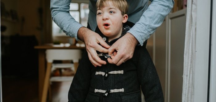 Man leaning over to do up young boy's duffel coat