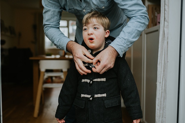 Man leaning over to do up young boy's duffel coat