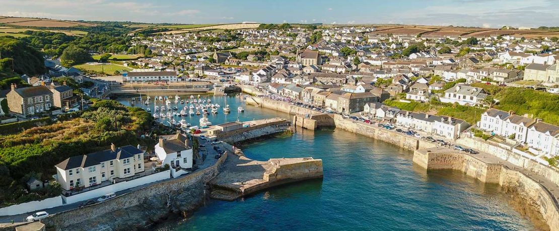 A bright blue sea flowing into a narrow harbour with pretty cottages all around