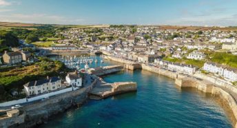 A bright blue sea flowing into a narrow harbour with pretty cottages all around