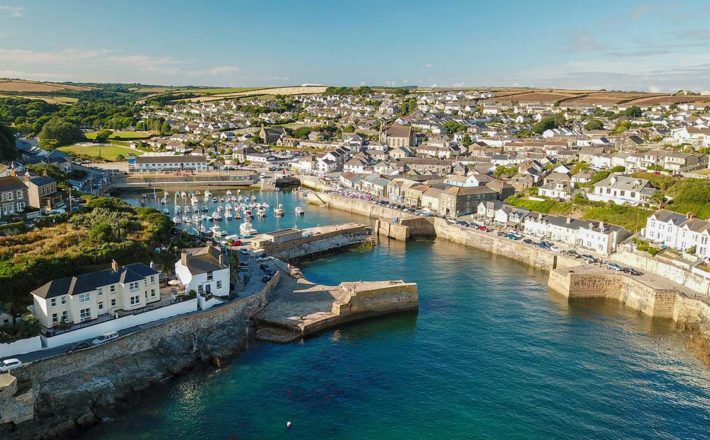 A bright blue sea flowing into a narrow harbour with pretty cottages all around