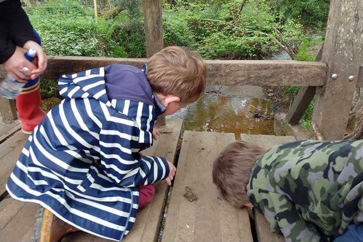 Two small boys kneel on a wooden bridge and look down