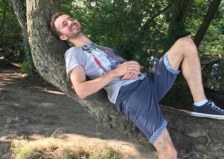 A man leans back into a tree on a riverbank