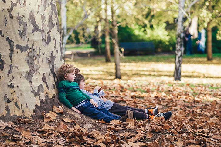 Small children lean against a tree in a park
