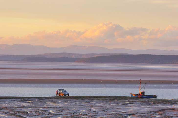 A wide flat stretch of beach with pinky orange skies