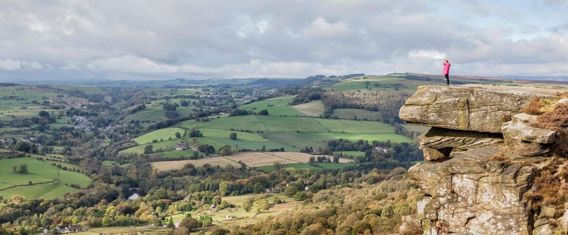 A person on a rocky outcrop viewing a valley landscape