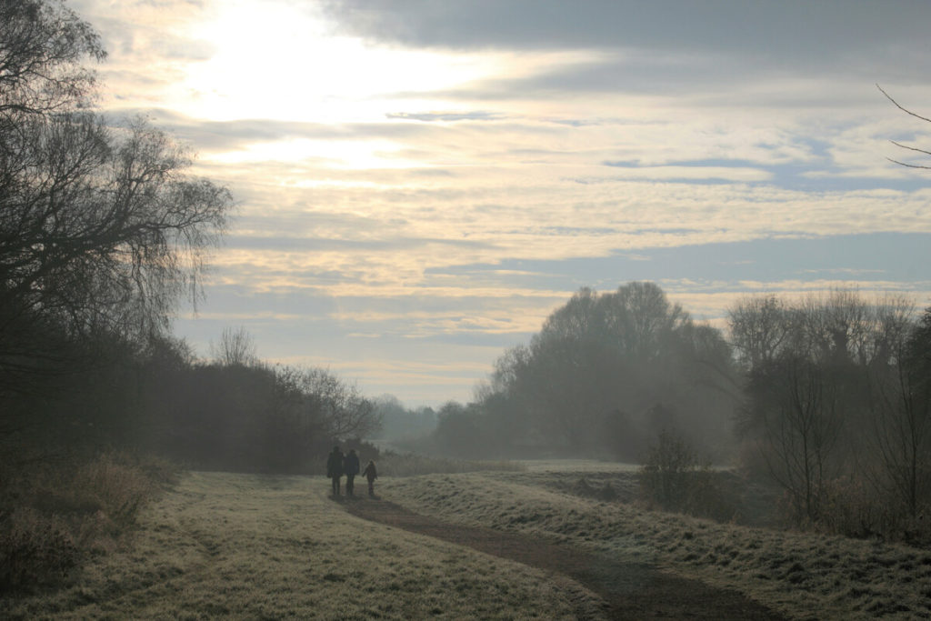 A family in distance out for a walk on a frosty and misty morning beside a river.