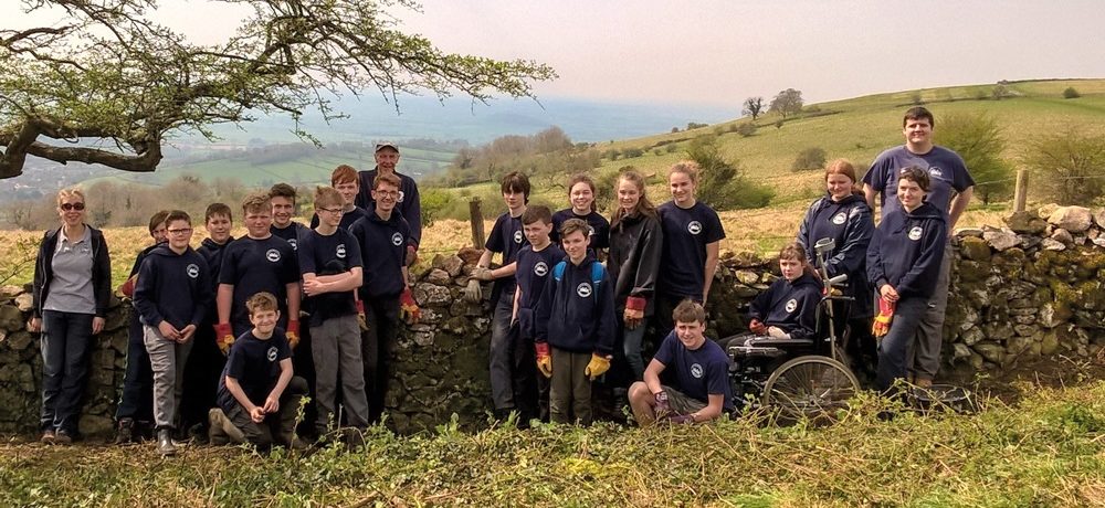 A group of young people standing by a dry stone wall in a rolling landscape