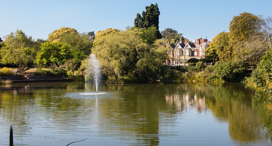 View across lake on sunny day to large Victorian house