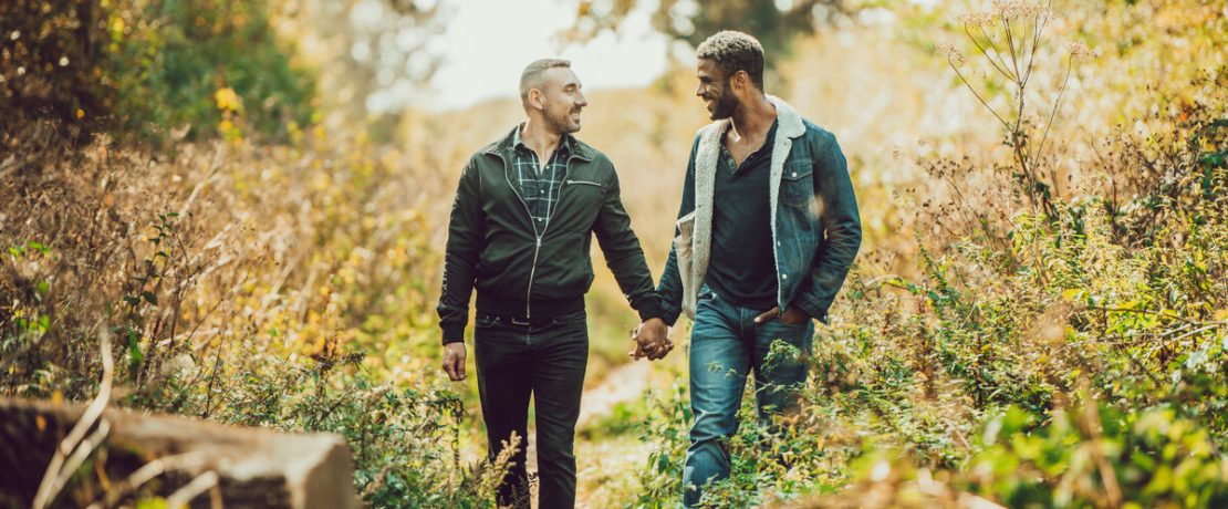 Two men holding hands walking along a country path among trees and hedges in autumn