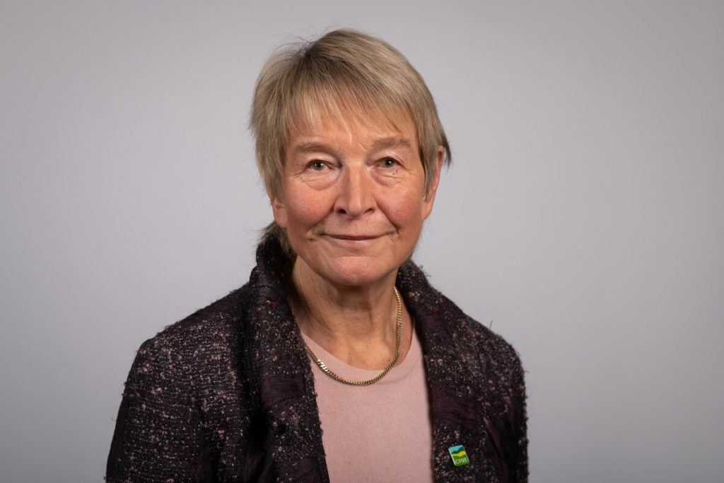 Head and shoulders of older woman with short fair hair and dark jacket smiling at camera