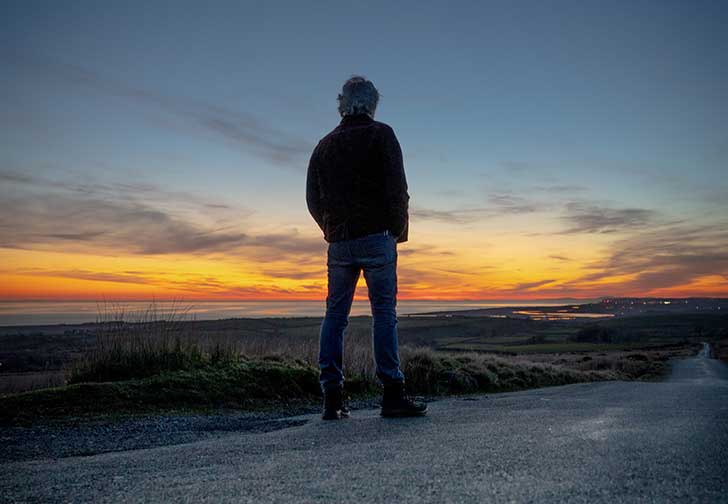 A man stands silhouetted against a dramatic sunset view