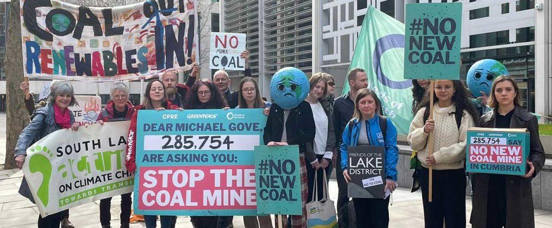 A row of people holding banners against coal power outside an office building