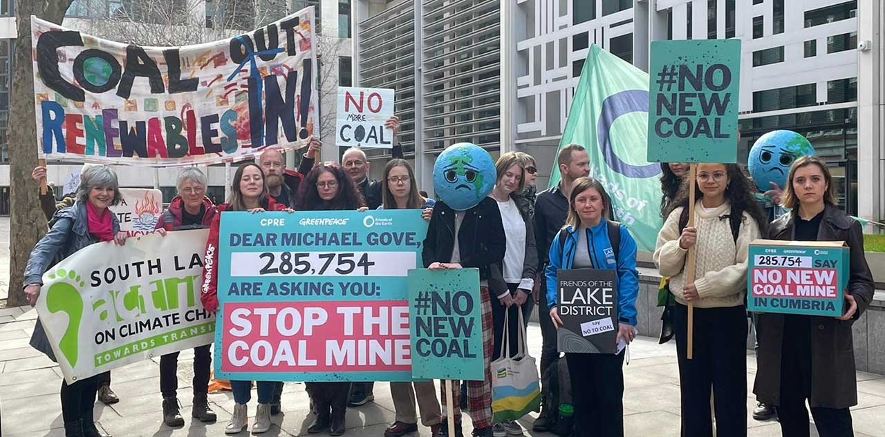 A row of people holding banners against coal power outside an office building