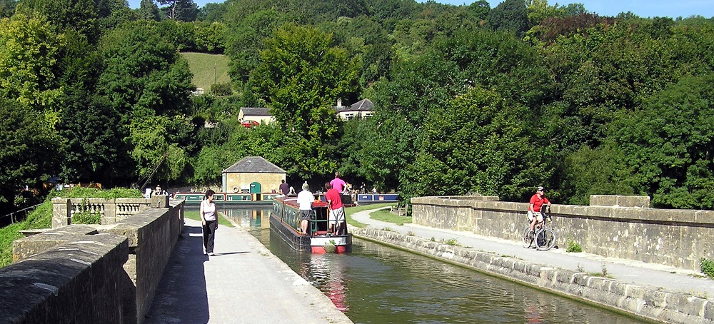 a walker, cyclist and barge on a canal on an aqueduct surrounded by green trees