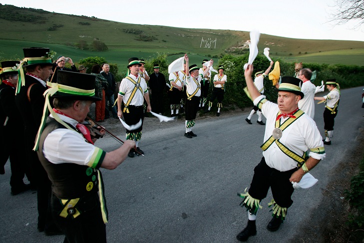 Morris men on road with long man chalked into hillside behind them.