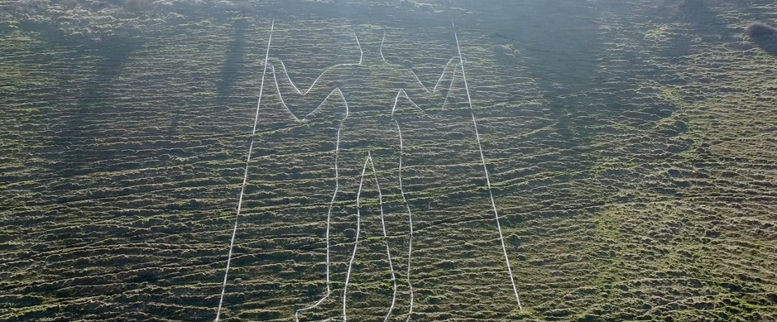 Chalk figure with sticks in both hands on hillside.