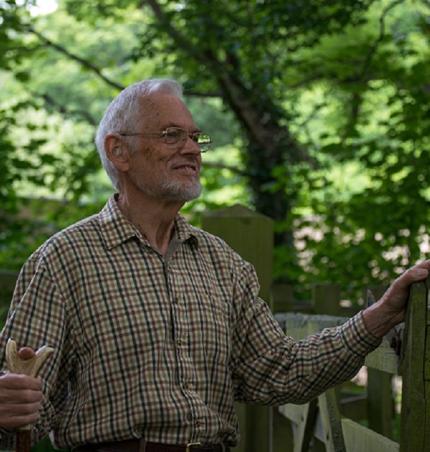 Older man in checked shirt with hand on fence