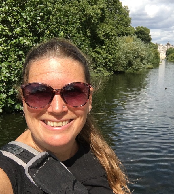 Head and shoulders of young woman with sunglasses on and lake behind her.