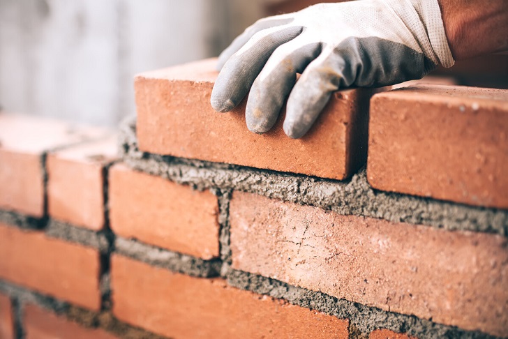 Close up of industrial bricklayer installing bricks on construction site.