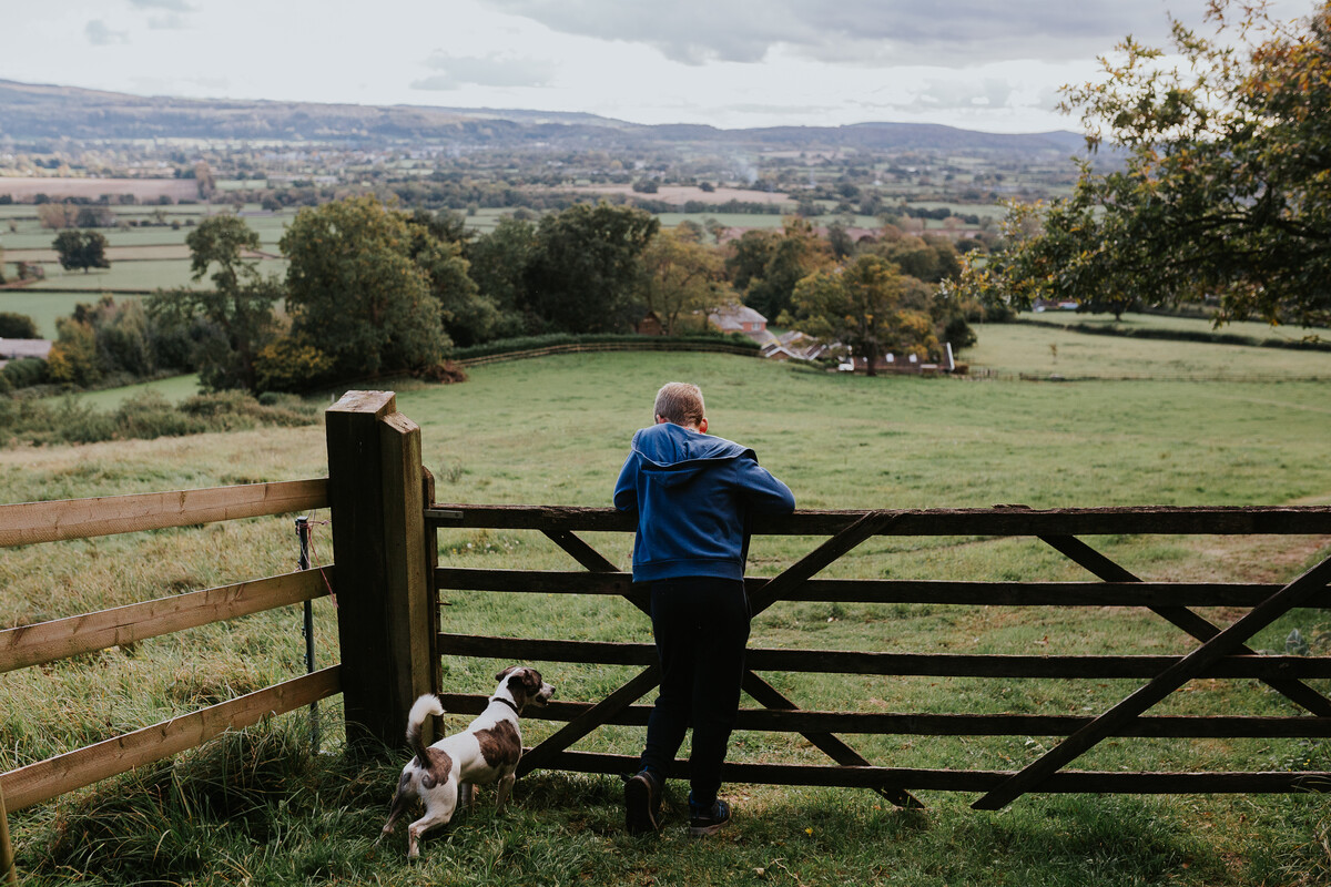 Child and a dog leaning against a wooden gate in a farm field