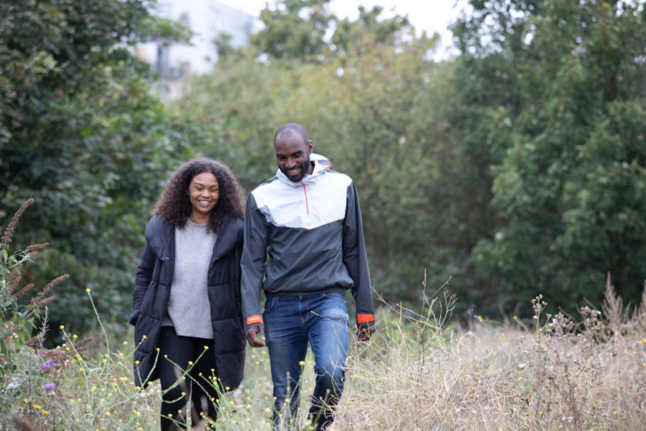 Couple in coats walking through overgrown grass area looking happy