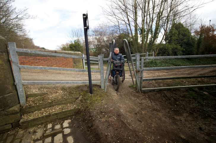 Man in wheelchair attempting to pass through a rural obstacle used to prevent bikes