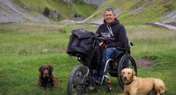 A man in wheelchair in the countryside with two dogs