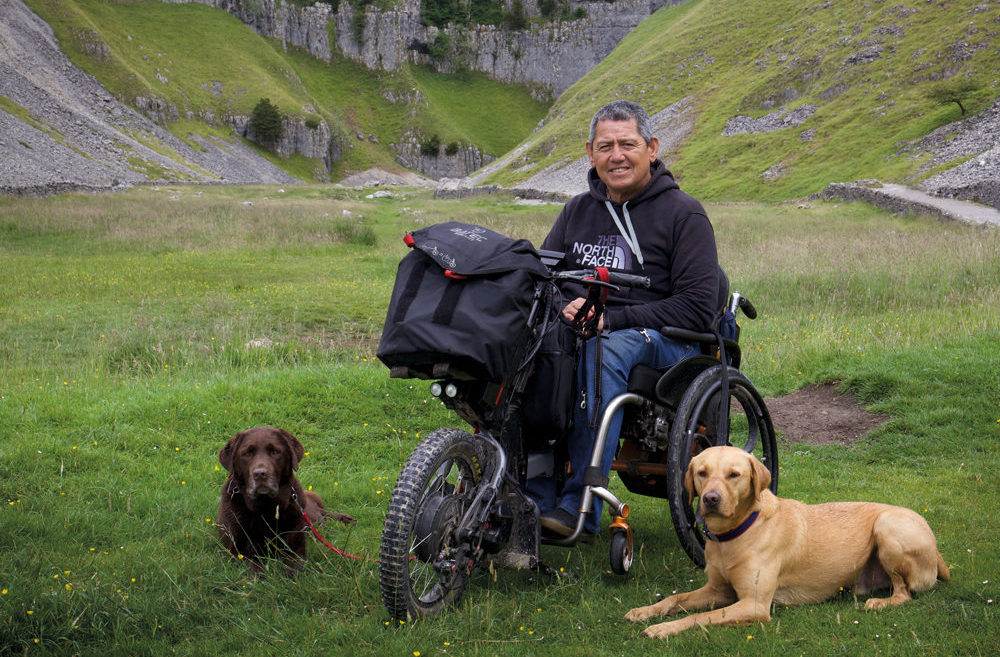A man in wheelchair in the countryside with two dogs