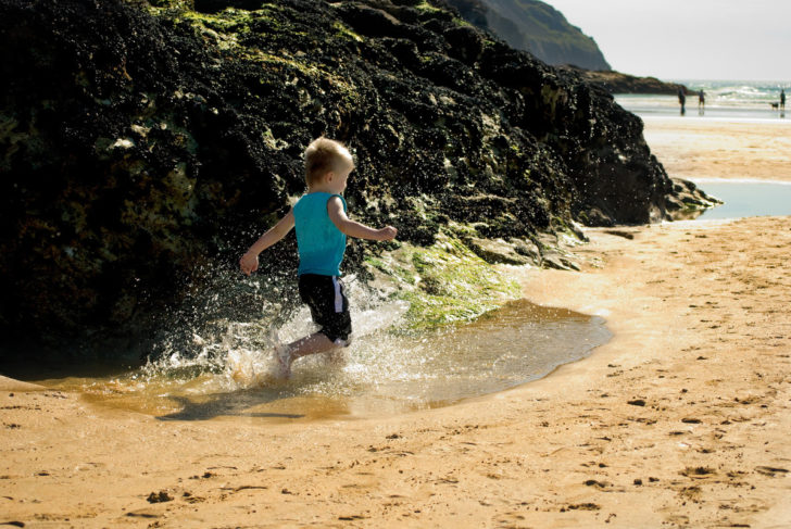 Boy runs through rock pools in Cornwall