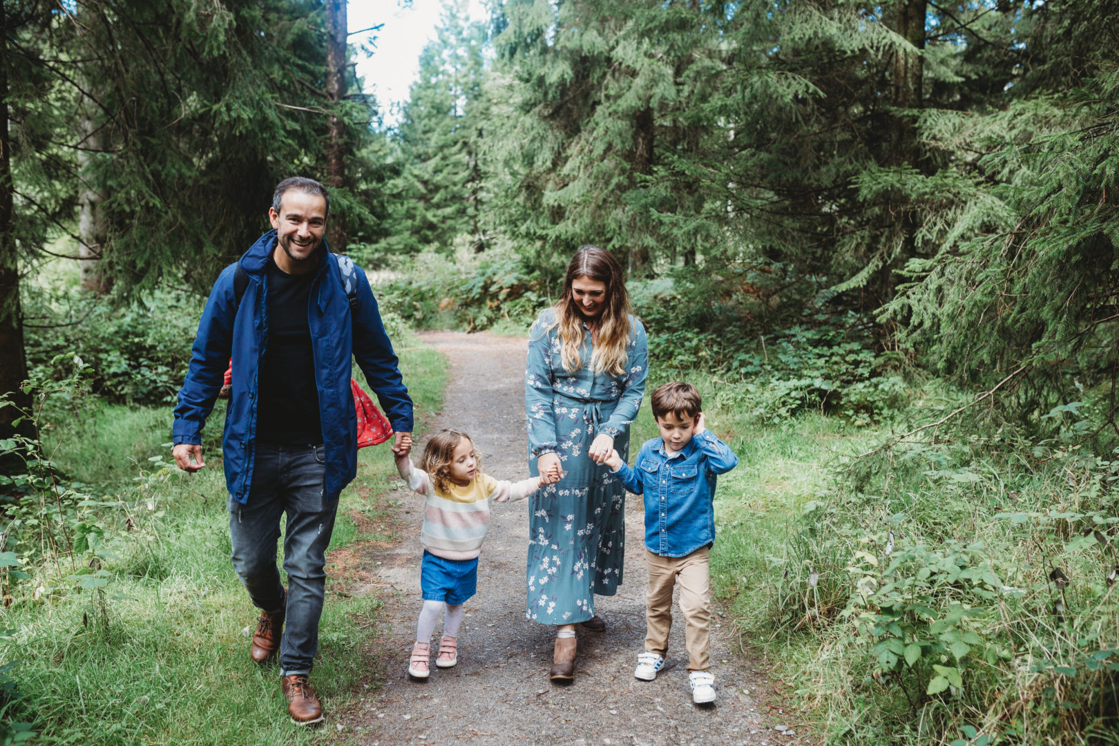 Young family holding hands walking on a path in the woods