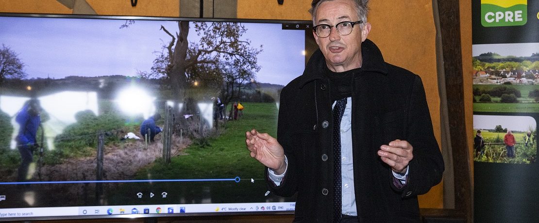 Man speaking in front of CPRE logo and screen showing hedgerow pictures.