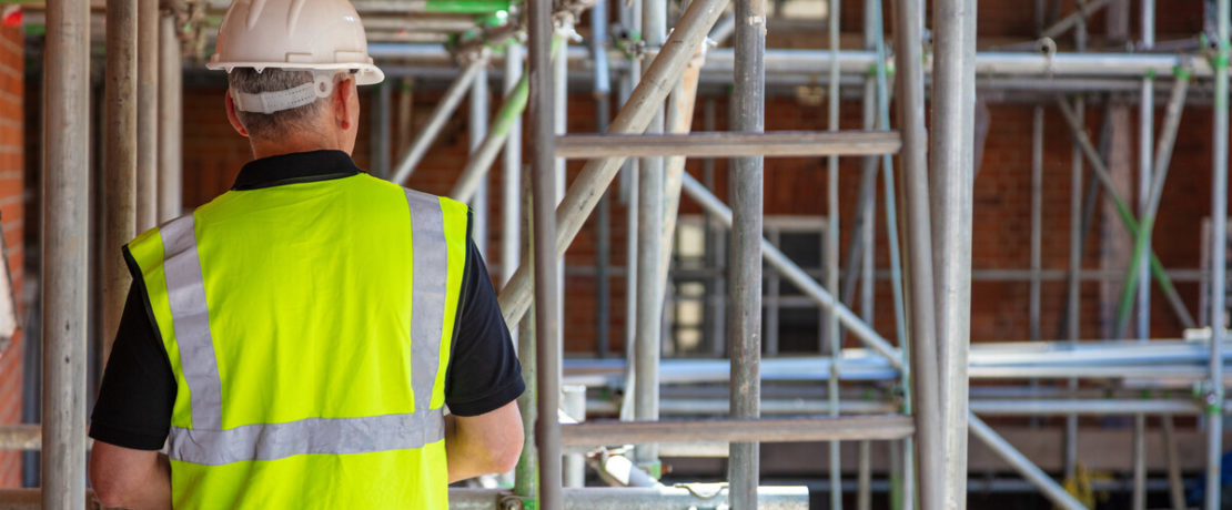 Rear view of male builder construction worker contractor on building site wearing hard hat and hi-vis yellow vest