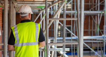 Rear view of male builder construction worker contractor on building site wearing hard hat and hi-vis yellow vest