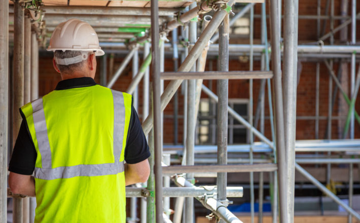Rear view of male builder construction worker contractor on building site wearing hard hat and hi-vis yellow vest