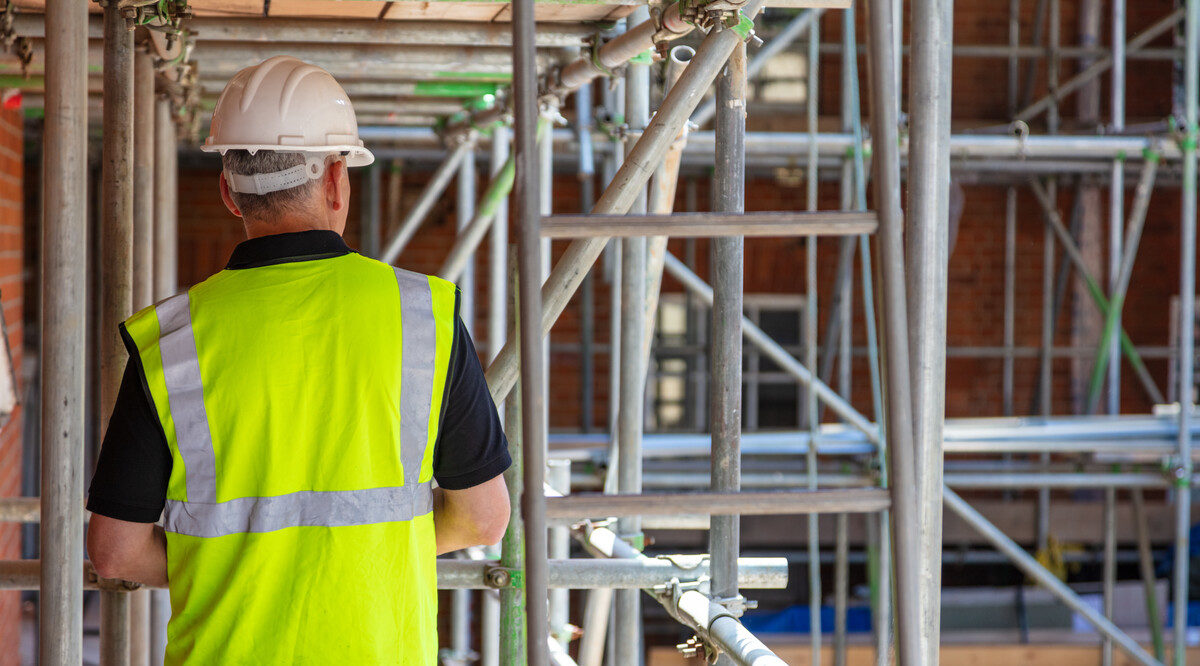 Rear view of male builder construction worker contractor on building site wearing hard hat and hi-vis yellow vest