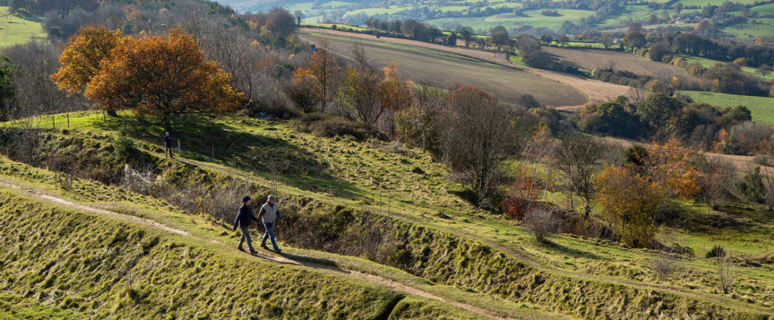 Man and women walking along a path with a big countryside view of farm fields and trees
