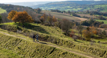 Man and women walking along a path with a big countryside view of farm fields and trees