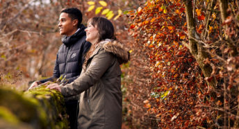 Woman and man leaning on dry stone wall and laughing