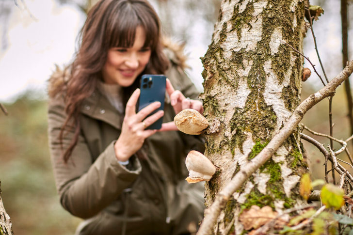 Woman taking picture of fungi on smartphone and smiling