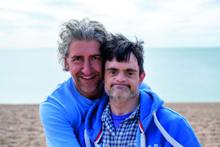 Two men embracing with a coastal view behind them 