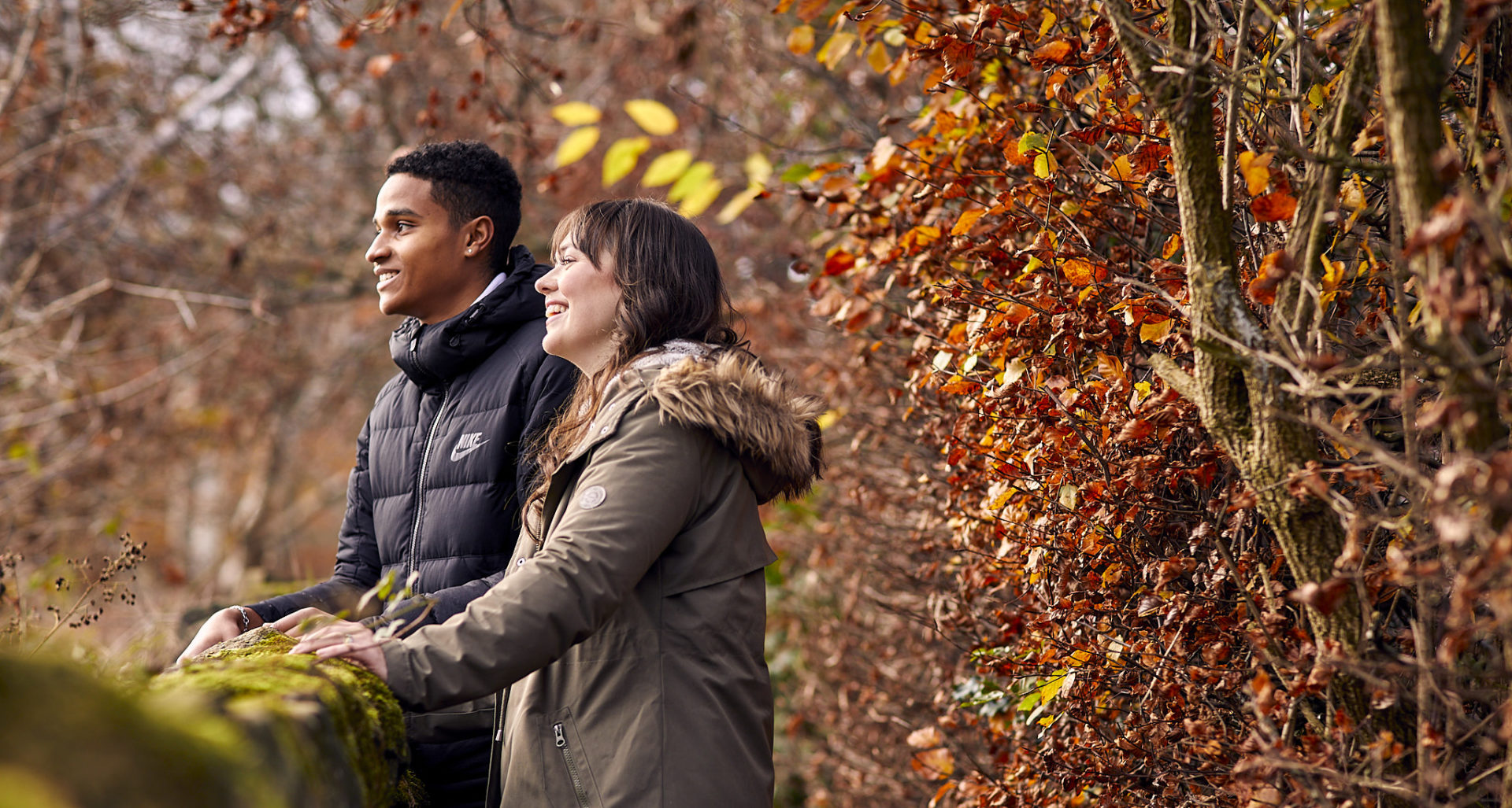 Woman and man leaning on dry stone wall and laughing