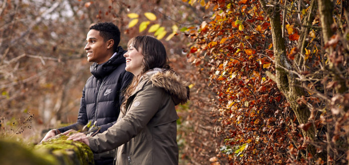 Woman and man leaning on dry stone wall and laughing