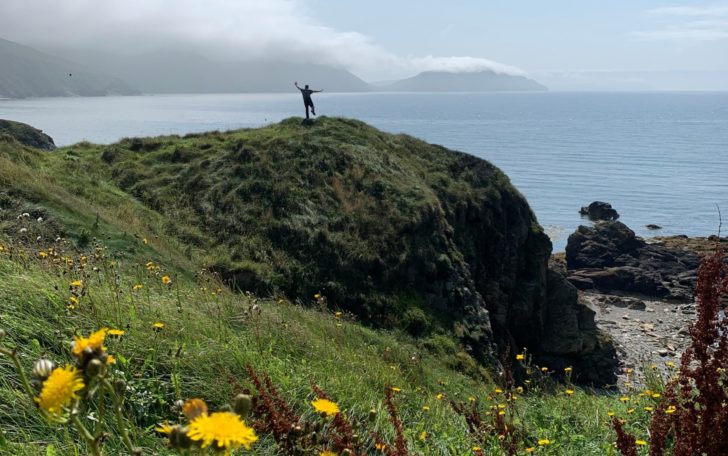 A man stood on top of a rocky hill overlooking the sea