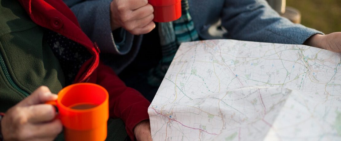 Women's hands holding mugs of coffee with a map spread out in front of them.