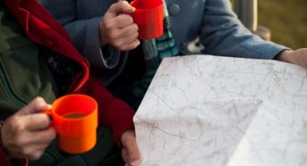 Women's hands holding mugs of coffee with a map spread out in front of them.